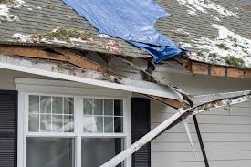 Storm-damaged homes with a torn-off roof and debris scattered across the yard after a hurricane